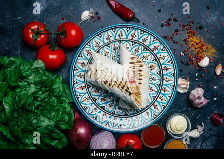 Döner Kebab (shawarma o döner wrap). Pollo alla griglia su lavash (pane pita) con verdure fresche - pomodori, insalata verde, peperoni. Vecchio backgr in legno Foto Stock