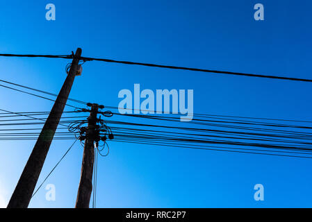 I poli con elettricità e cavi per telecomunicazioni visto da sotto contro il cielo blu sullo sfondo. Foto Stock