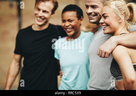 Diversi gruppi di amici in sportswear in piedi sotto braccio in una palestra e sorridente dopo una classe di allenamento insieme Foto Stock