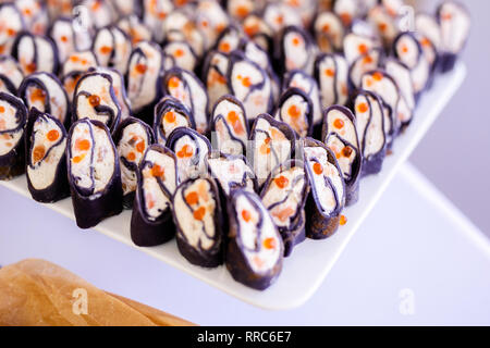 Rotoli di frittelle di nero con formaggio, salmone e caviale rosso sulla piastra bianca, bella presentazione. Foto Stock