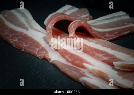 Close up materie dry-cured back bacon su una pietra scura piatto Foto Stock