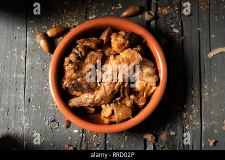 Angolo di alta vista di una casseruola di terracotta con alcuni pezzi di coniglio, di prugne e di funghi, tipicamente consumato in Spagna, il grigio di una tavola in legno rustico Foto Stock