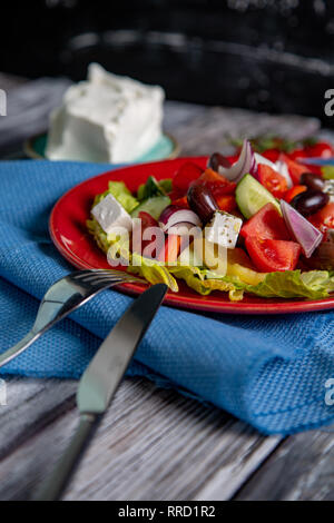 Insalata greca di cetriolo fresco, pomodoro, peperoni dolci, lattuga, cipolla rossa, il formaggio feta e olive con olio di oliva su sfondo di legno. Cibo sano Foto Stock