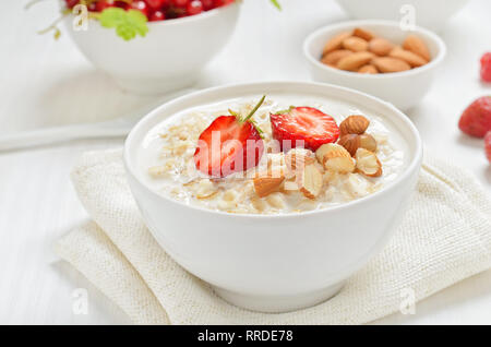 Farina di avena porridge con fette di fragola e i dadi nella ciotola sul tavolo bianco Foto Stock