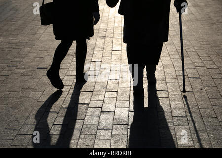 Ragazza e la donna con una canna da zucchero, silhouette nera e le ombre di due persone che camminano per la strada. Concetto di zoppicante, vecchiaia, anziani o non vedente Foto Stock