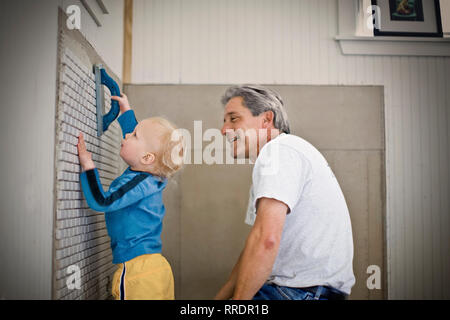 Mid-adulto uomo sorridente mentre si guarda il suo giovane figlio di aiuto con comodo lavorare dentro la loro casa. Foto Stock