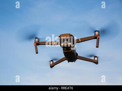 Un basso angolo di visione di un futuristico quadcopter drone in volo con quattro eliche di tornitura e drone in bilico contro un cielo blu sullo sfondo Foto Stock
