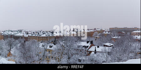 Città urbana vista delle vecchie case da una collina nella città di Stoccolma in una nebbiosa giornata invernale con la neve sui tetti e sugli alberi, Svezia Foto Stock