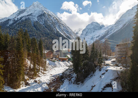 DOMBAY, RUSSIA, febbraio 28, 2018: vista del fiume di montagna e alberghi sullo sfondo delle montagne del Caucaso in inverno giornata di sole Foto Stock