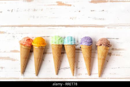 Vista superiore del arcobaleno colorato coni gelato bianco su sfondo di legno. Concetto di estate Foto Stock