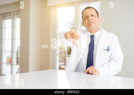 La mezza età medico uomo indossa cappotto medico presso la clinica cercando infelice e arrabbiato che mostra il rifiuto e negativo con il pollice verso il basso gesto. Bad expres Foto Stock