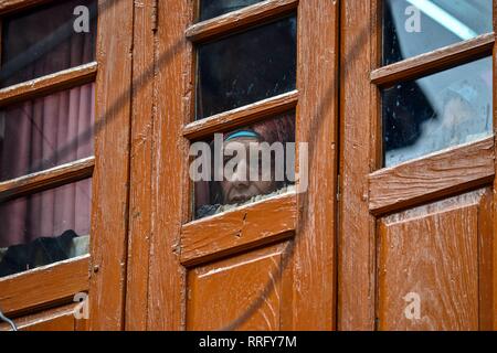 Febbraio 26, 2019 - Srinagar, J&K, India - una donna guarda fuori dalla finestra come membri dell'Intelligenza indiano ufficiali (non illustrato) lascia la casa del top leader separatista Yasin Malik, dopo un raid a Srinagar Kashmir. La National Investigation Agency (NIA) Martedì effettuate ricerche su top leader separatista in Kashmir la valle in un terrore finanziamenti case, hanno detto i funzionari. Il NIA funzionari sono stati accompagnati dalla polizia locale e CRPF. Nel frattempo, scontri scoppiati in località Maisuma subito dopo sleuths delle indagini nazionali Agenzia effettuato incursioni su top leader separatista. (Credito Ima Foto Stock