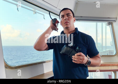 Navigazione pilota offcier sul ponte di una nave in corso con bicnocular e radio. La linea di orizzonte e belle nuvole su uno sfondo. Foto Stock