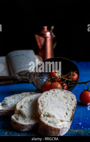 Composizione di pomodori ciliegia e fette di pane su legno schede blu su sfondo nero Foto Stock