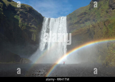 Persona in rainbow sotto 60m-alta cascata Skogafoss. Skogar, Sudhurland, sud dell'Islanda. Foto Stock