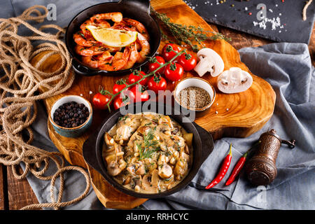 Gran fritto di gamberi in salsa di pomodoro con olio di oliva,funghi in salsa di panna julienne, champignon, prodotti per la cottura sul tavolo di legno sfondo Foto Stock