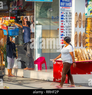 L'uomo carico di un cesto su una testa portante donna in Kuta Bali Indonesia. Foto Stock