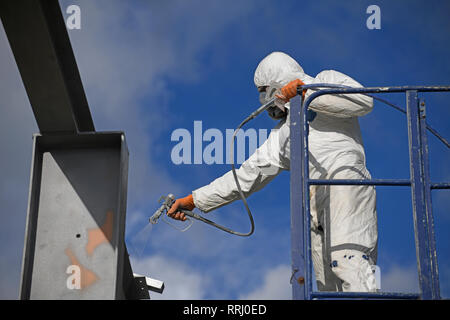 Tradesman vernici spray travi in acciaio su un sito in costruzione Foto Stock