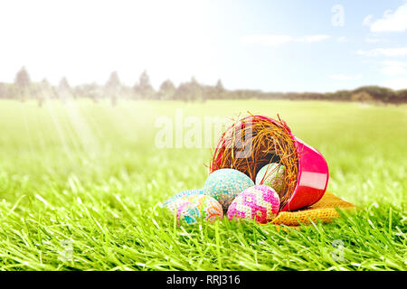 Colorate le uova di pasqua spillato dal nido in rosso la benna con tessuto sul campo verde con alberi e cielo blu sullo sfondo. Buona Pasqua Foto Stock