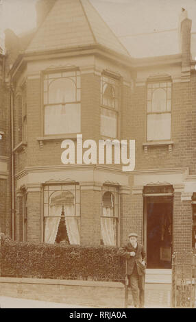 Vintage Cartolina fotografica che mostra una giovane Edwardian uomo in piedi alla porta di casa Pavenhill, Harcourt Road, Wood Green, Londra, Inghilterra. Foto Stock