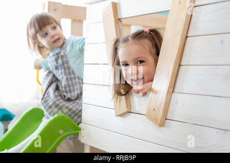 Carino bambino bambina guarda fuori dalla finestra del giocattolo di legno casa e sorrisi. Foto Stock