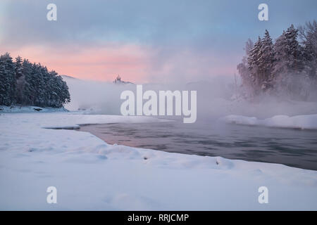 Paesaggio invernale e l'hotel, che sorge sulla riva di un fiume congelato, metà nascosto dalla nebbia dal fiume a giù. Fiume di Katun, montagne di Altai, Foto Stock