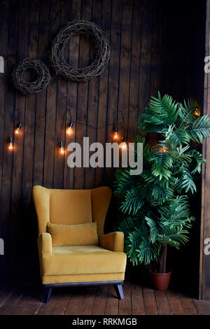 Accogliente centro senape-poltrona colorata, Palm tree e pareti di legno. Interno in stile retrò. Caldo giallo garland luce . Foto Stock