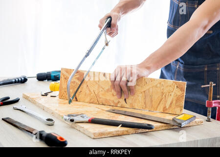 Carpenter operando con cautela guardando i piani di lavoro in falegnameria. Egli è imprenditore di successo al suo posto di lavoro. martellare un chiodo supporta sulla build Foto Stock