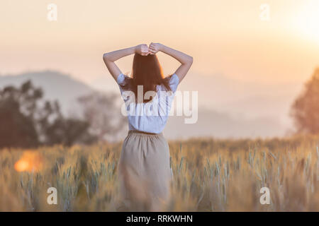 Bella donna asiatica divertendosi al campo di orzo in estate al tramonto Foto Stock