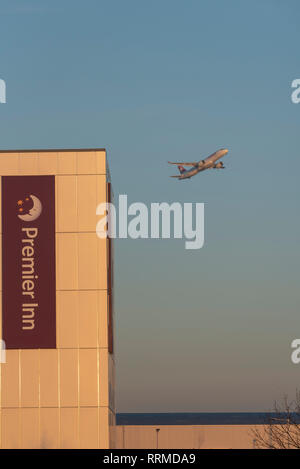 Aereo Jet aereo decollo dall'Aeroporto Heathrow di Londra, Regno Unito, passando Premier Inn hotel in alba mattina. Compagnia aerea precoce della partenza del volo. Luce rossa Foto Stock