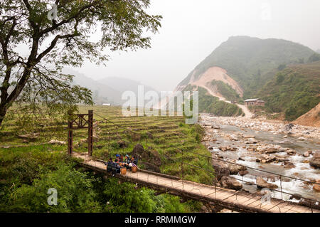 Un gruppo di donne Hmong in abbigliamento tradizionale di sedersi su un ponte di legno da un campo a gradini e il fiume, Sa Pa, Vietnam Foto Stock