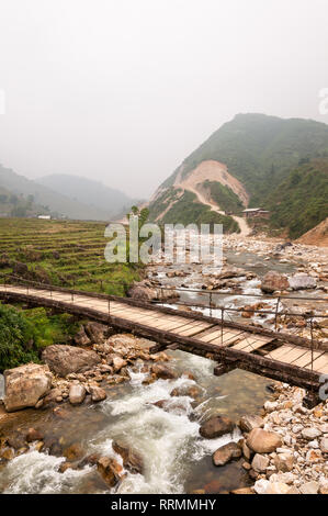 Un ponte di legno su un fiume con le colline in background su un nebbioso giorno, Sa Pa, Vietnam Foto Stock