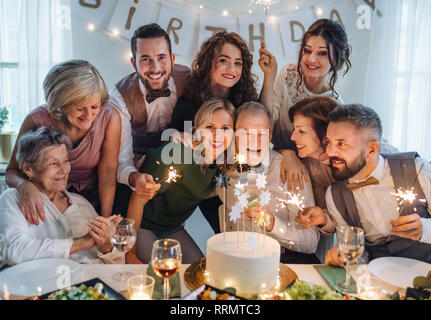Un uomo anziano con famiglia multigenerazionali e una torta festeggia il compleanno su una parte interna. Foto Stock