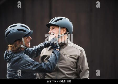 Attivo felice coppia senior con caschi moto in piedi all'aperto contro uno sfondo scuro. Foto Stock