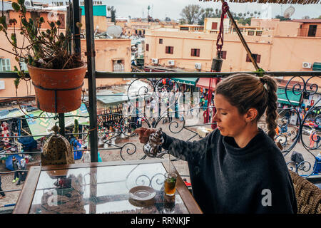 Donna godendo di Tè sul balcone che si affaccia sulla strada del mercato, Marrakech, Marocco Foto Stock