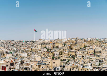 Bandiera giordana volando sopra la soleggiata città di edifici, Amman, Giordania Foto Stock