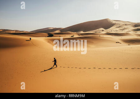 Uomo che cammina nella soleggiata, deserto sabbioso, Sahara, Marocco Foto Stock