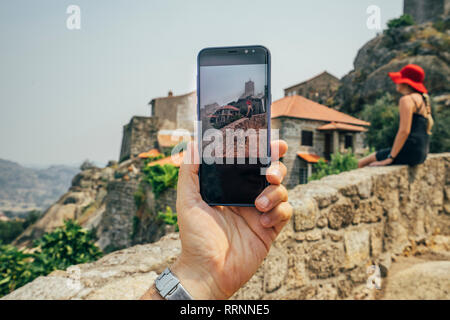 Personale prospettiva uomo con la fotocamera del telefono a fotografare la donna sul muro di pietra, Monsanto, Portogallo Foto Stock