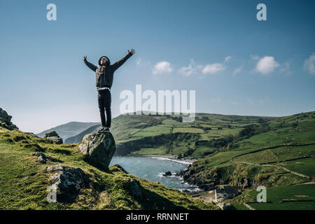 Carefree uomo in piedi sulla roccia che si affaccia soleggiato, paesaggio idilliaco, Irlanda del Nord Foto Stock