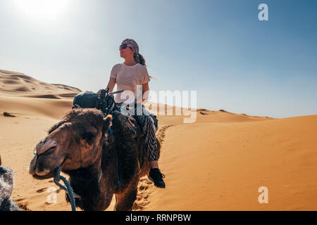 Equitazione donna camel nella soleggiata deserto sabbioso, Sahara, Marocco Foto Stock