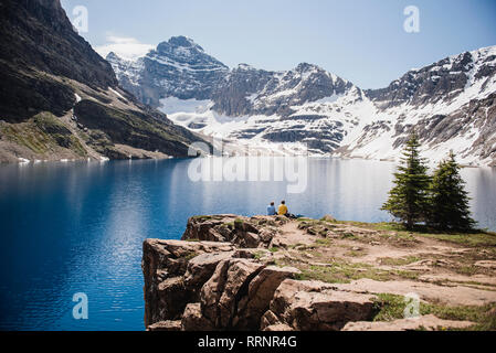 Giovane seduto sulla scogliera che si affaccia sulla tranquilla e soleggiata montagna e lago, Yoho Park, British Columbia, Canada Foto Stock