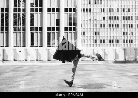 L'uomo ballando con ombrello in testa al di fuori di edifici urbani Foto Stock