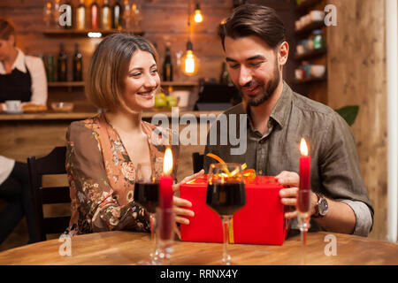 Giovane uomo cercando felice dopo riceve un regalo da parte sua fidanzata. Uomo bello guardare grati al suo compleanno. Foto Stock