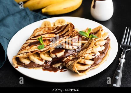 Gustosa crêpe con granella di nocciole cioccolato da spalmare e banana sulla piastra bianca Foto Stock