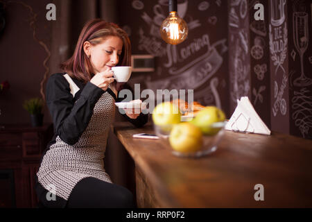 Donna adulta gode la sua tazza di caffè presso il bar contatore. Donna relax nel vintage coffee shop Foto Stock