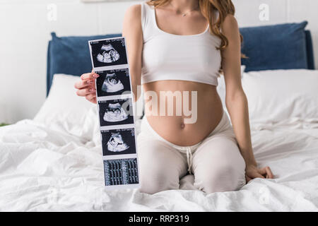 Vista ritagliata della donna incinta seduta sul letto e mostra le scansioni a ultrasuoni Foto Stock