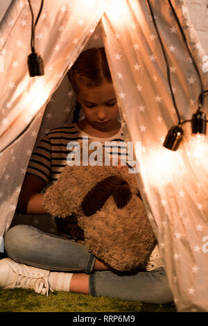 Preteen kid gioca con Teddy in barba wigwam con le lampadine Foto Stock