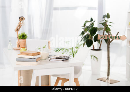 Area di lavoro con libri e computer portatile vicino andare segno verde in ufficio moderno, risparmio ambientale concetto Foto Stock