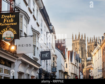 Gli edifici e i cartelli lungo Petergate con York Minster nella distanza della città di York Yorkshire Inghilterra Foto Stock