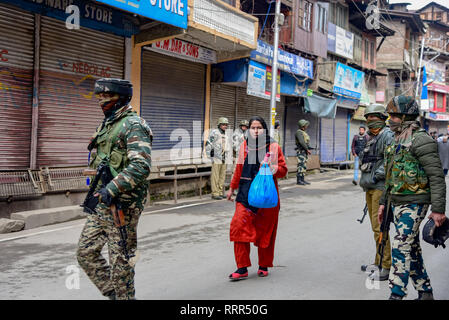 Una donna del Kashmir vedere a piedi passato paramilitari indiano troopers permanente sulla protezione al di fuori di casa del leader separatista Yasin Malik durante il raid di indagine nazionale agenzia (NIA). Le forze indiane in Indian amministrato il Kashmir usato gas lacrimogeni gusci per sedare la protesta contro le incursioni sui principali leader separatista da Indiana funzionari di intelligence. Foto Stock